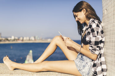 Young pretty woman wearing beach wear sitting on wall - GIOF02352