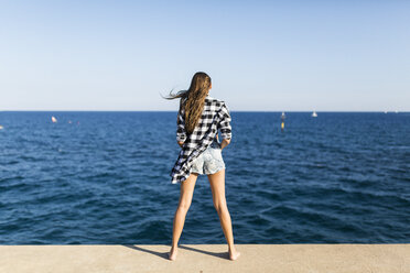 Young woman standing at the sea, rear view - GIOF02359