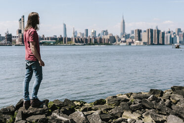 USA, New York City, Mann steht am Wasser mit der Skyline von Manhattan im Hintergrund - GIOF02404