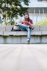 Man sitting on a bench with earbuds using cell phone - GIOF02411