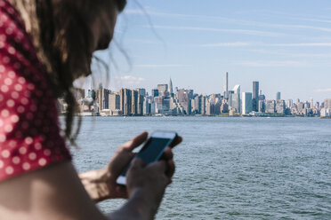 USA, New York City, man using cell phone with Manhattan skyline in background - GIOF02413