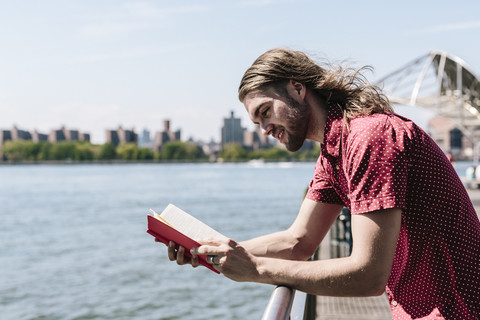USA, New York City, Mann liest Buch am Hafen, lizenzfreies Stockfoto