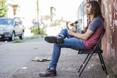 USA, New York City, man sitting on a chair using cell phone in Williamsburg, Brooklyn - GIOF02429