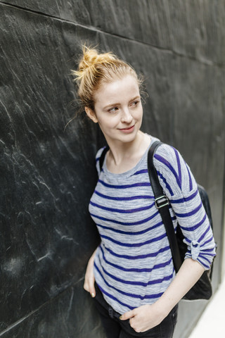 Smiling young woman standing at a wall outdoors stock photo