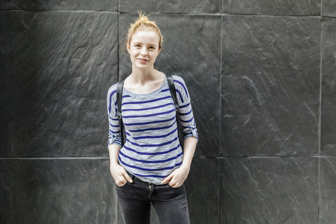 Porträt einer lächelnden jungen Frau, die an einer Mauer im Freien steht, lizenzfreies Stockfoto