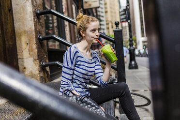 USA, New York City, woman sitting on stoop drinking a smoothie in Manhattan - GIOF02440