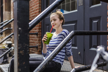 USA, New York City, woman sitting on stoop drinking a smoothie in Manhattan - GIOF02443