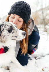 Young woman kissing her dog in the snow - MGOF03078