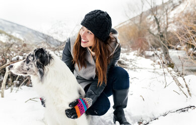 Junge Frau spielt mit ihrem Hund im Schnee - MGOF03080