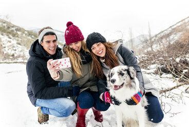 Drei Freunde haben Spaß daran, ein Selfie mit einem Hund im Schnee zu machen - MGOF03086