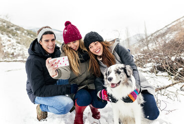 Three friends having fun taking a selfie with a dog in the snow - MGOF03086