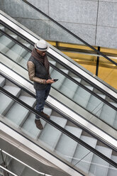 Junger Mann steht auf Rolltreppe und schaut auf sein Handy - MAUF00994