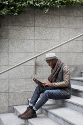 Mann sitzt auf einer Treppe und benutzt ein Tablet - MAUF01002