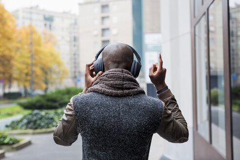 Rückenansicht eines glatzköpfigen Mannes, der mit Kopfhörern Musik hört - MAUF01005