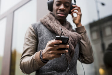 Mann mit Glatze hört Musik mit Kopfhörern und schaut auf sein Handy, Nahaufnahme - MAUF01006