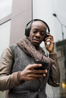 Mann mit Glatze hört Musik mit Kopfhörern und schaut auf sein Handy - MAUF01007