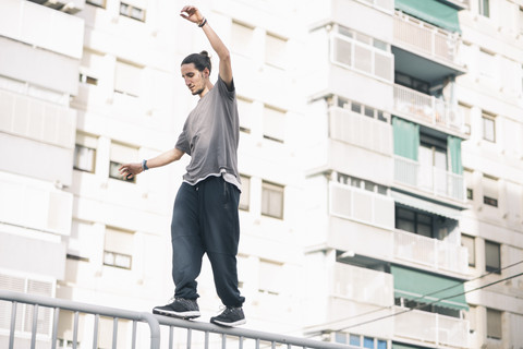 Junger Mann macht Parkour in der Stadt und balanciert auf einem Geländer, lizenzfreies Stockfoto