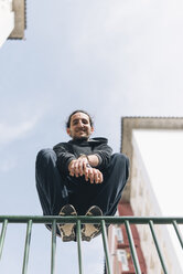 Junger Mann beim Parkour in der Stadt auf dem Geländer hockend - SKCF00276