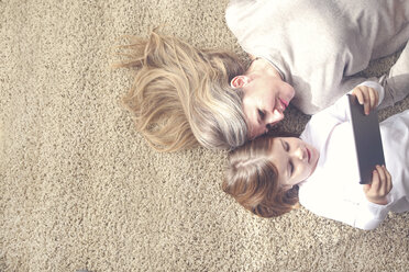 Mother and daughter lying on carpet looking at tablet - RTBF00751