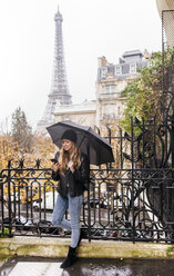 Frankreich, Paris, junge Frau benutzt ihr Smartphone mit dem Eiffelturm im Hintergrund - MGOF03099