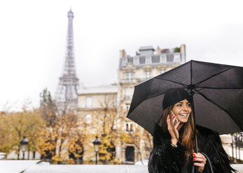 Frankreich, Paris, junge Frau telefoniert unter Regenschirm mit dem Eiffelturm im Hintergrund - MGOF03103