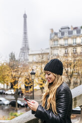 Frankreich, Paris, junge Frau benutzt ihr Smartphone mit dem Eiffelturm im Hintergrund - MGOF03108