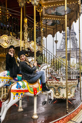 Frankreich, Paris, zwei beste Freunde fahren auf einem Karussell mit dem Eiffelturm im Hintergrund - MGOF03114