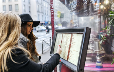 Frankreich, Paris, zwei Touristinnen beim Durchblättern der Speisekarte eines Restaurants - MGOF03122