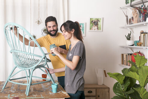 Young couple painting wicker armchair in blue at home - RTBF00777