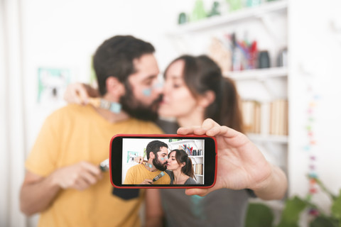 Junges Paar, das sich küsst und ein Selfie mit Pinseln macht, lizenzfreies Stockfoto