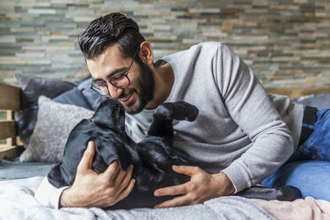 Lächelnder Mann, der mit seinem Hund zu Hause auf der Couch kuschelt - TCF05324