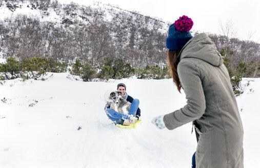 Mann und Frau haben Spaß mit Schlitten und Hund im Schnee - MGOF03134