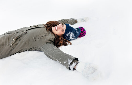 Lächelnde junge Frau, die im Schnee liegt - MGOF03136