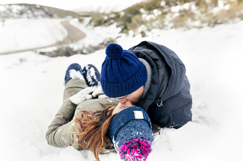 Junges Paar, das sich im Schnee küsst, lizenzfreies Stockfoto