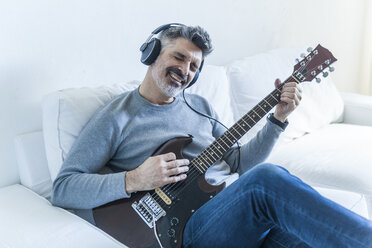 Älterer Mann spielt zu Hause E-Gitarre und trägt Kopfhörer - TCF05334