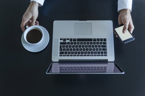 Draufsicht auf einen Geschäftsmann am Schreibtisch mit Laptop, Smartphone und einer Tasse Kaffee - TCF05358