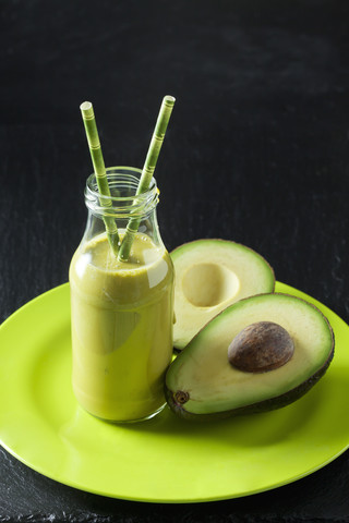 Glasflasche mit Avocado-Smoothie und geschnittener Avocado auf einem Teller, lizenzfreies Stockfoto