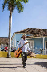 Cuba, walking man with guitar and stool on the street - MAUF01030