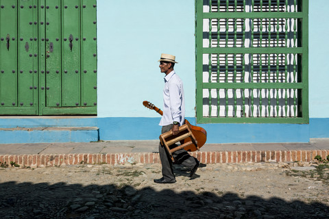 Kuba, Trinidad, gehender Mann mit Gitarre und Hocker auf der Straße, lizenzfreies Stockfoto