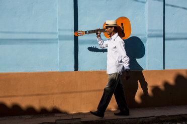 Cuba, man with guitar walking on the street - MAUF01037