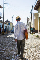 Cuba, Trinidad, back view of man with guitar walking on the street - MAUF01040