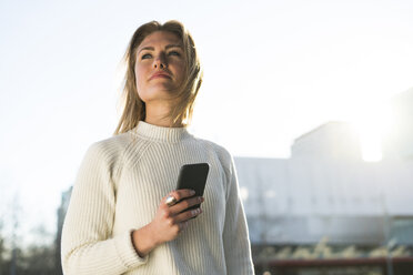 Portrait of young woman with cell phone looking at distance - KKAF00545