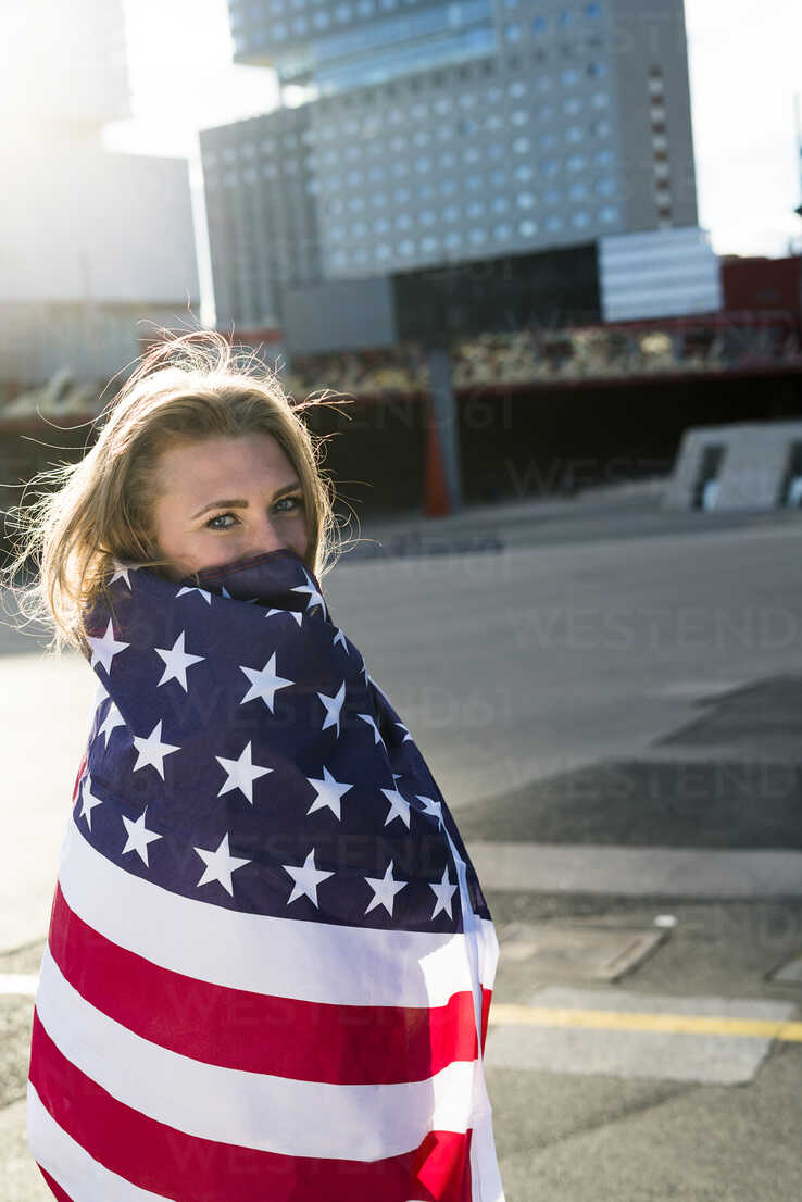 Side view of confident young ethnic lady in sports bra waving American flag  and looking at camera against modern glass skyscraper stock photo