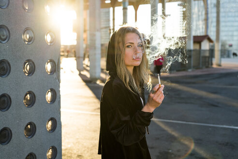 Porträt einer blonden jungen Frau, die eine Zigarette raucht - KKAF00551