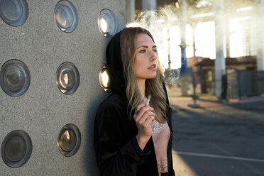 Porträt einer blonden jungen Frau, die bei Gegenlicht eine Zigarette raucht - KKAF00553