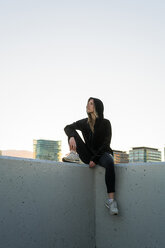 Spanien, junge, schwarz gekleidete Frau, die auf einer Mauer sitzt und in die Ferne schaut - KKAF00567