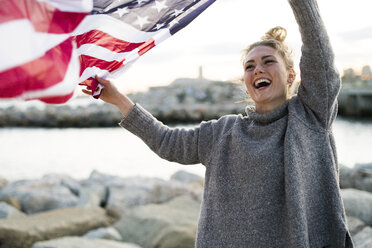 Porträt einer lachenden jungen Frau, die eine US-amerikanische Flagge weht - KKAF00576