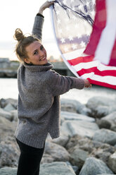 Porträt einer lächelnden jungen Frau mit wehender US-amerikanischer Flagge - KKAF00577