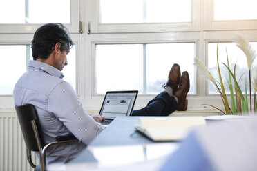 Mann mit Laptop am Fenster im Büro - FKF02208