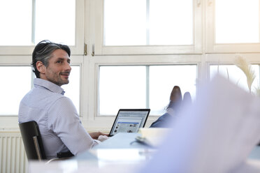 Mann mit Laptop am Fenster im Büro - FKF02209